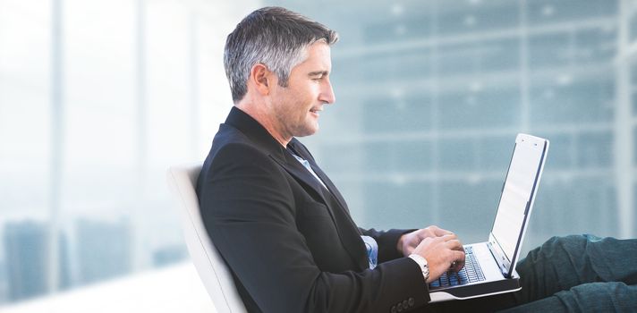 Businessman using laptop against modern room overlooking city