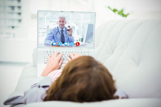 Doctor holding medicine jar against woman using laptop while lying on sofa