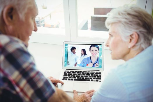 Confident nurse standing upright accompanied by her team in the background against senior couple using laptop