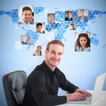 Smiling businessman using laptop at desk against background with hexagons and world map
