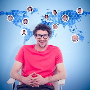 Happy businessman wearing reading glasses while sitting on chair against background with hexagons and world map
