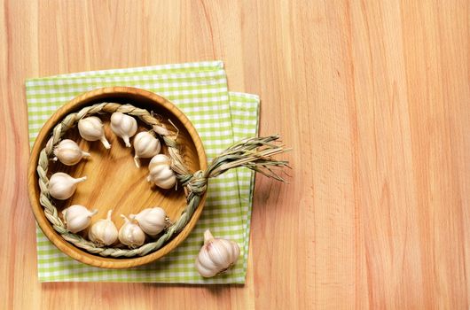 Braid of garlic in wooden plate on a fabric green plaid cloth on a light wooden table.