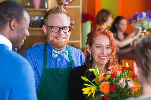 Male owner smiles with employee and customer in a busy flower shop