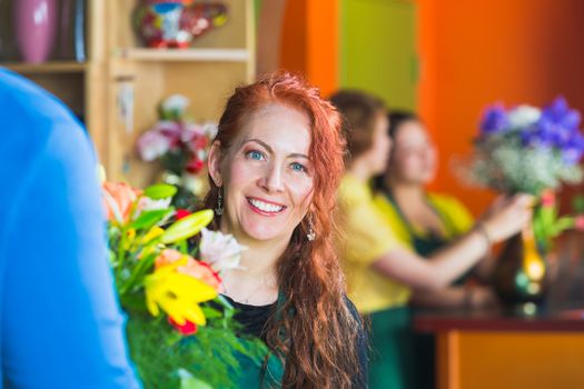Pretty woman with customer smiling in a busy flower shop