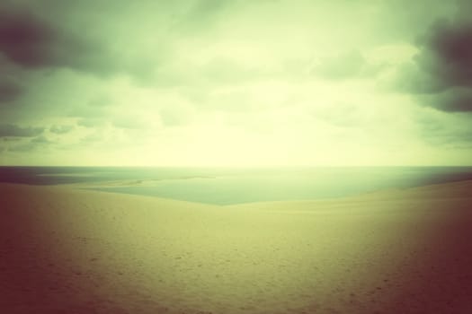 Dark misty landscape with sand dunes, clouds and sea.