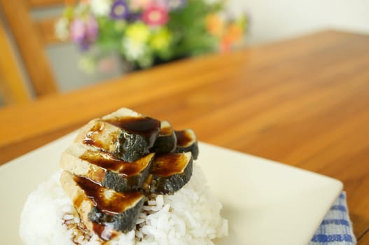 Vegetarian fried salted fish slice pour sauce and white rice with blue fabric on wood table and blur flower as background.