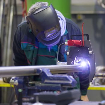 Industrial operator setting  computer controlled process of orbital welding machine in inox pipes manufacturing workshop.