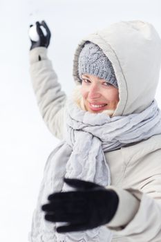 Cute casual young woman throwing snowball in winter time.