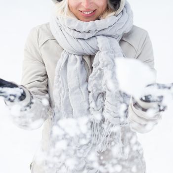 Cute casual young woman playing with snow in winter time.