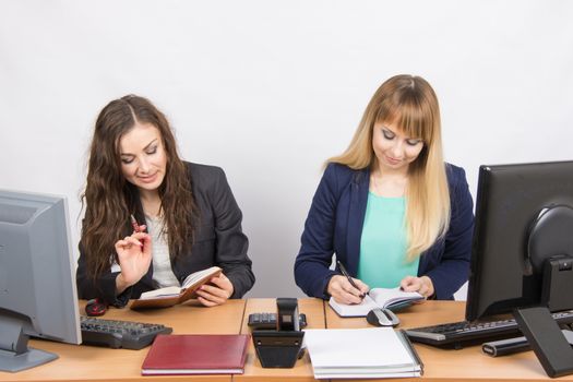 Two young pretty business woman sitting at a office table is divided into two jobs