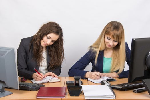 Two young pretty business woman sitting at a office table is divided into two jobs