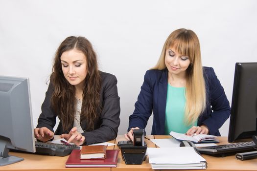 Two young pretty business woman sitting at a office table is divided into two jobs
