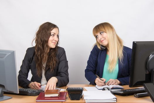 Two young pretty business woman sitting at a office table is divided into two jobs