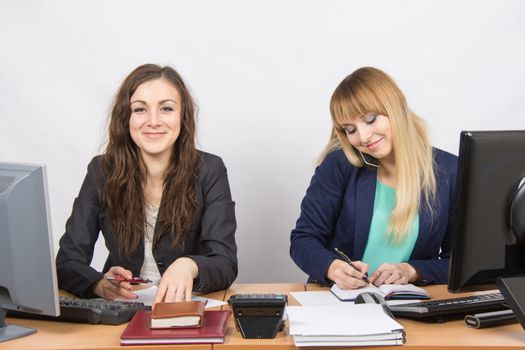 Two young pretty business woman sitting at a office table is divided into two jobs