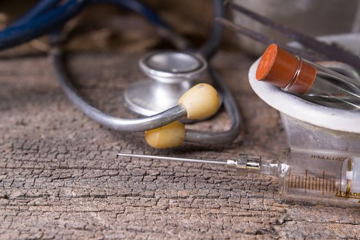 Old medical syringes , hypodermic needles and stethoscope on old wood background