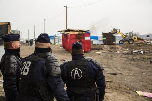FRANCE, Calais: Riot police officers stand guard as agents dismantle shacks and shelters in the Jungle migrant camp, in the French northern port city of Calais, on March 1, 2016. Workers were due to start a second day of destruction in the southern half of the camp, where thousands of migrants and refugees have been living while they try to reach Britain.