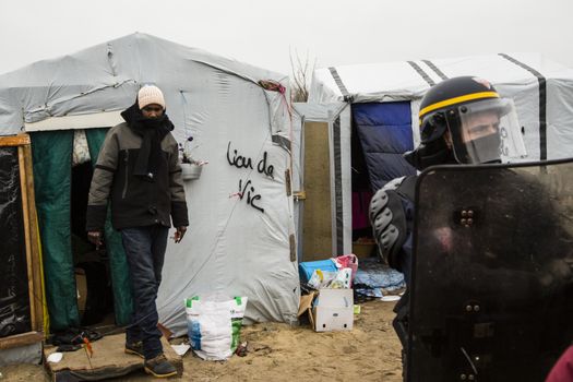 FRANCE, Calais: A riot police officer stands guard as agents dismantle shacks and shelters in the Jungle migrant camp, in the French northern port city of Calais, on March 1, 2016. Workers were due to start a second day of destruction in the southern half of the camp, where thousands of migrants and refugees have been living while they try to reach Britain.
