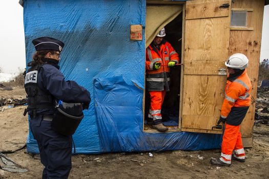 FRANCE, Calais: A police officer stands next to agents dismantling a shack in the Jungle migrant camp, in the French northern port city of Calais, on March 1, 2016. Workers were due to start a second day of destruction in the southern half of the camp, where thousands of migrants and refugees have been living while they try to reach Britain.