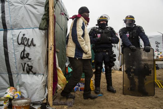 FRANCE, Calais: Riot police officiers stand guard next to a migrant as agents dismantle shacks in the Jungle migrant camp, in the French northern port city of Calais, on March 1, 2016. Workers were due to start a second day of destruction in the southern half of the camp, where thousands of migrants and refugees have been living while they try to reach Britain.