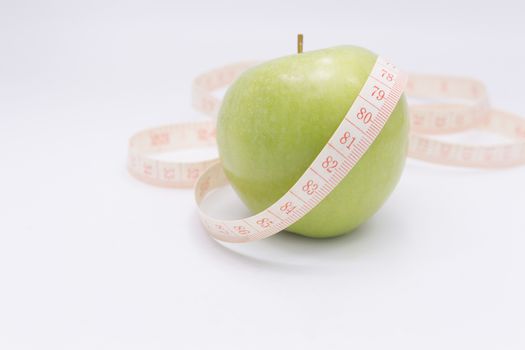 A green apple with a measuring tape wrapped around it for the concept of dieting.