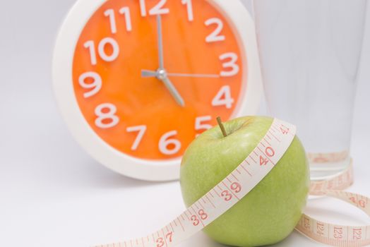 A green apple with a measuring tape wrapped around it and orange clock  for the concept in dieting and time to start