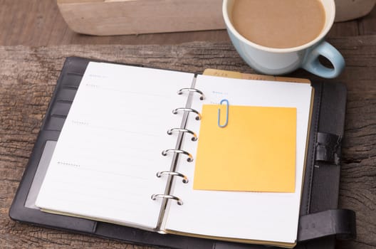 Weekend concept. Pink rose, mug with coffee, diary and stcky notel on a wooden table. Selective focus, copy space background