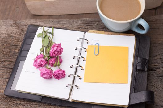 Weekend concept. Pink rose, mug with coffee, diary and stcky notel on a wooden table. Selective focus, copy space background