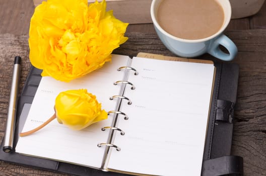 Weekend concept. yellow flowers, mug with coffee, diary and pencil on a wooden table. Selective focus, copy space background