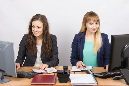 Two young pretty business woman sitting at a office table is divided into two jobs