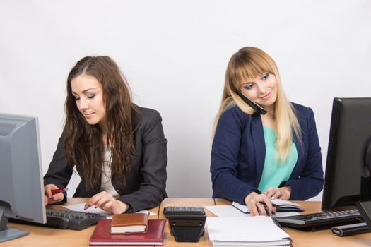 Two young pretty business woman sitting at a office table is divided into two jobs