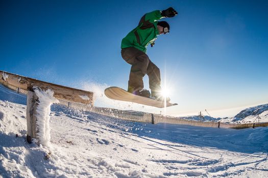 Snowboarder jumping from a wood rail against blue sky.