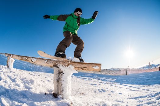 A snowboarder executes a radical slide on a rail in a snow park.