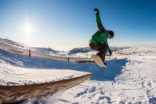 Snowboarder jumping from a wood rail against blue sky.