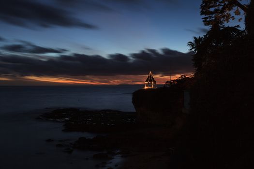 A gazebo on a cliff overlooking the ocean in Laguna Beach, California, lit with Christmas lights at sunset.