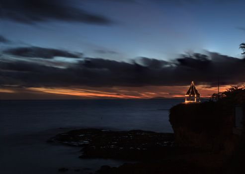 A gazebo on a cliff overlooking the ocean in Laguna Beach, California, lit with Christmas lights at sunset.
