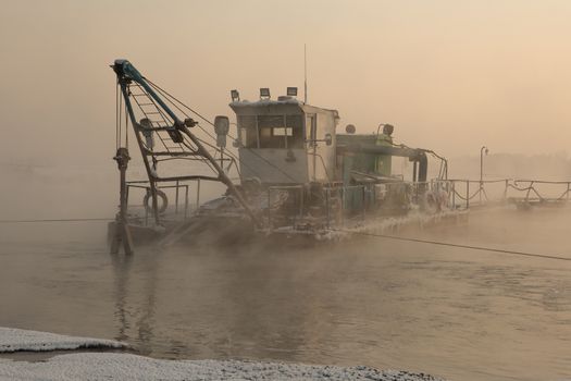 a dredger boat in winter mist at sunset