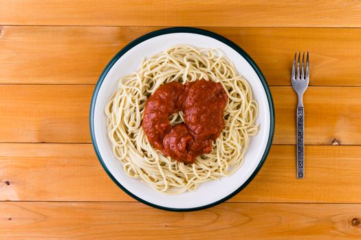 Overhead view of a plate of Italian spaghetti pasta served with a savory tomato sauce on a wooden garden table for a tasty lunch