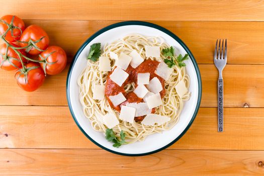 Plate of healthy Italian spaghetti pasta topped with a savory tomato sauce and cheese garnished with parsley on a wooden table with fresh tomatoes