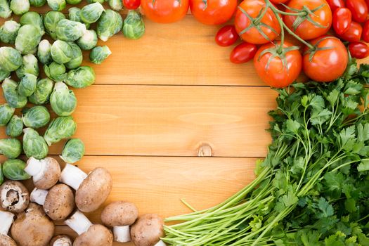 Healthy border of fresh vegetables for cooking on a wooden table with brussels sprouts, tomatoes, parsley and baby bella mushrooms around a central round copy space