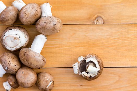 Fresh organic baby bella mushrooms for use as a savory ingredient in cooking and salads on a wooden kitchen table, viewed from above