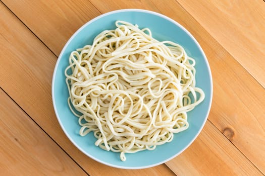 Plated of freshly boiled plain spaghetti served on a blue plate on a wooden garden table with diagonal planks, overhead view