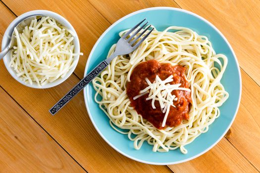 Italian spaghetti Bolognese garnished with grated gruyere cheese with a side dish containing additional cheese alongside, overhead view on a wooden table