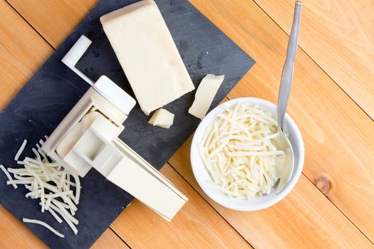 Preparing grated gruyere cheese for cooking with an overhead view of a rotary grater and wedge of cheese on a board alongside grated cheese in a bowl