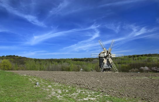 Spring landscape with a windmill in a plowed field with a blue sky and clouds on a sunny day. Ukraine.