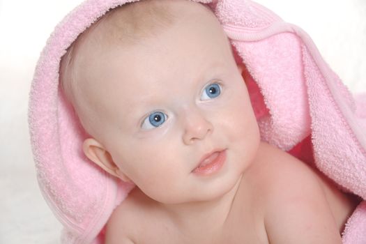 Adorable baby girl looking  under a pink towel