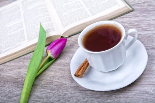 A cup of tea with cinnamon and purple tulip on a wooden background