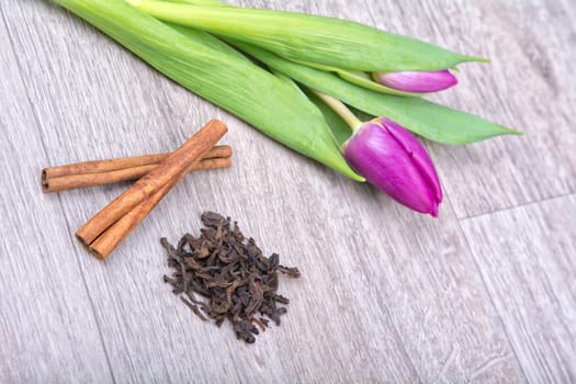 Cinnamon, tea, and purple tulips on a wooden background