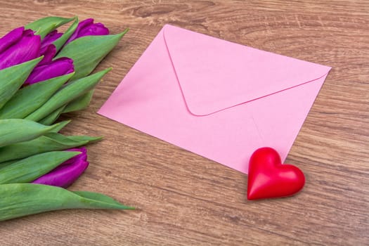 Pink envelope with red heart and purple tulips on a wooden background