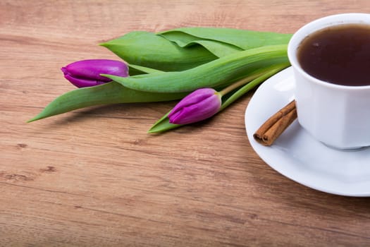 A cup of tea with cinnamon and purple tulips on a wooden background