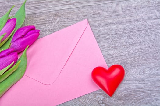 Pink envelope with red heart and purple tulips on a wooden background